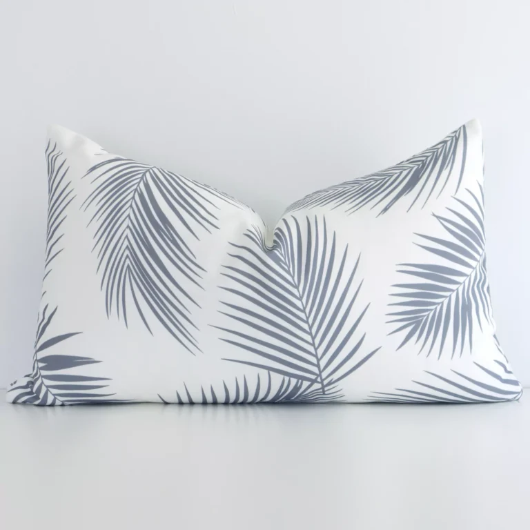 Outdoor rectangular cushion with a palm design in an upright position against a white wall. It is grey in colour.