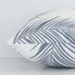 A sideways perspective of this palm-designed outdoor cushion. The positioning shows the border of the rectangular shape and the grey colour.