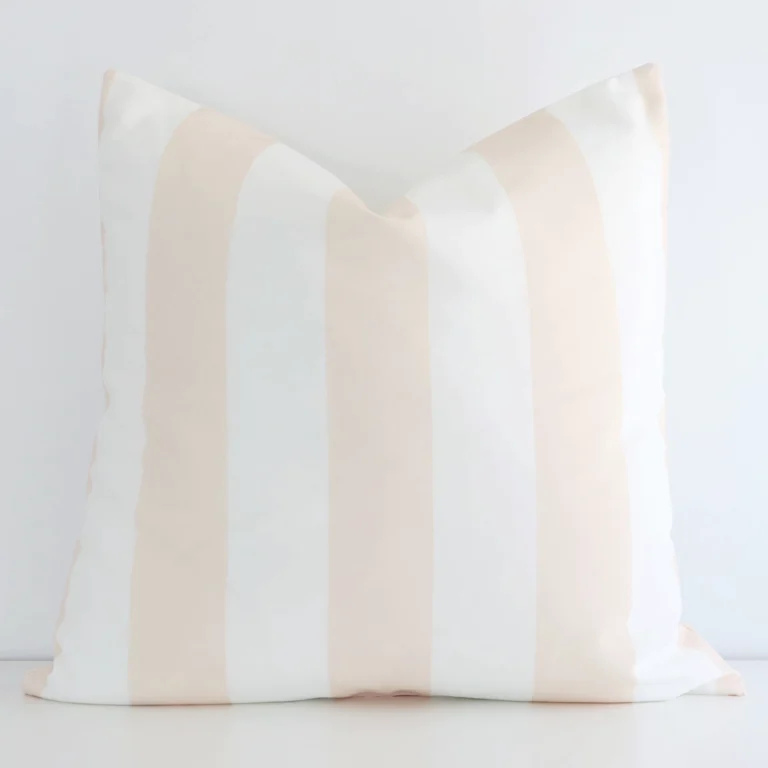 Beige cushion positioned in front of a white wall. It has large dimensions and is made from an outdoor material.