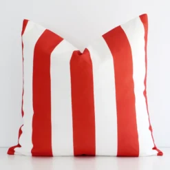 A white wall that has a striped red cushion cover positioned in front of it. It has an exquisite outdoor material and a lovely large size.