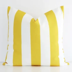 An outdoor large cushion cover that has a unique striped design is shown vertically against a white wall. It has a wonderful yellow colour.
