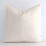 Here a beige outdoor cushion is shown styled against a white wall. It has a square design and features a solid-coloured style.