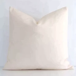 Here a beige outdoor cushion is shown styled against a white wall. It has a square design and features a solid-coloured style.