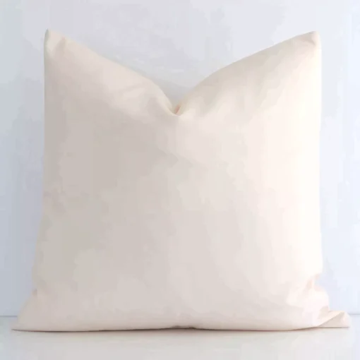 Here a beige outdoor cushion is shown styled against a white wall. It has a square design and features a solid-coloured style.