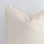 A zoomed in photo of the corner of a beige solid-coloured cushion that has an outdoor fabric and a square shape.