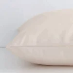 Square solid-coloured cushion in beige colour laying flat. The viewpoint highlights the seams of the outdoor fabric.