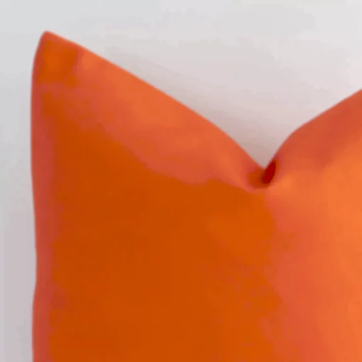 Cropped shot of top left corner of this solid-coloured orange cushion cover. This viewpoint shows the orange fabric and square shape with more precision.