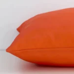 Bold orange cushion laid horizontally. This perspective shows the edge of the outdoor fabric and its square shape.
