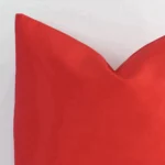 Very close photo of a bold red cushion. The shot shows the outdoor material and the corner of its square shape with more clarity.