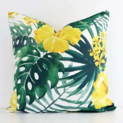 Square yellow cushion positioned in front of white brickwork. Its floral style pops on the outdoor fabric.