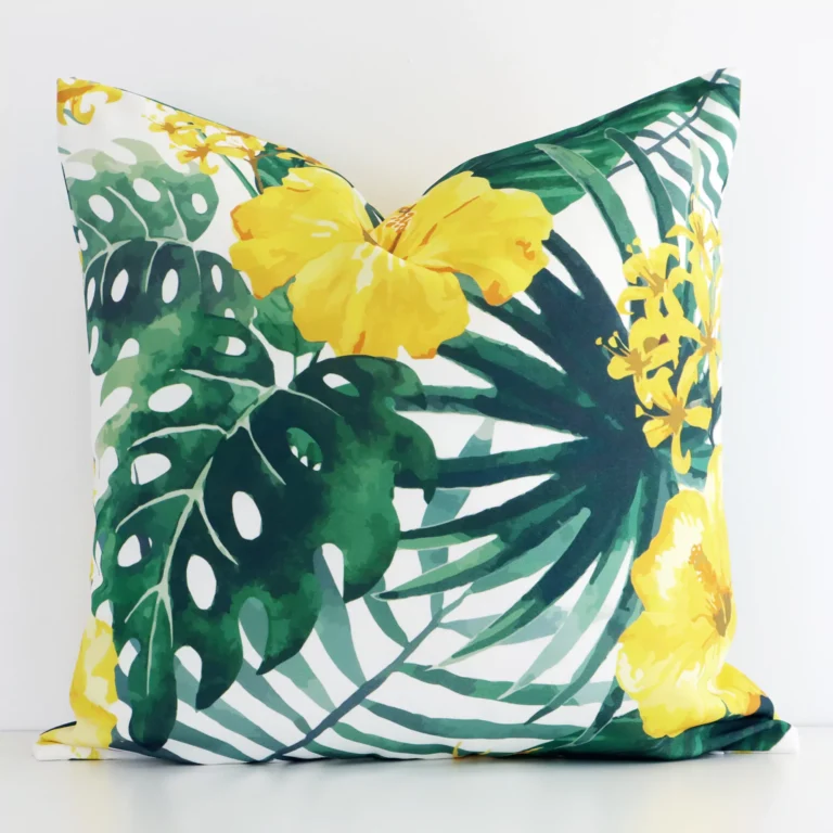 Square yellow cushion positioned in front of white brickwork. Its floral style pops on the outdoor fabric.