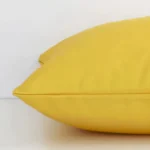 Side perspective showing seam of square solid-coloured yellow cushion cover that has a an outdoor fabric.