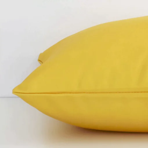 Side perspective showing seam of square solid-coloured yellow cushion cover that has a an outdoor fabric.