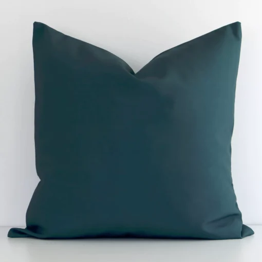 Dark green solid-colured cushion cover sits against a white wall. It is constructed from a superior looking linen material and has a square shape.
