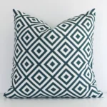 Green square cushion positioned in front of a white wall. It has geometric dimensions and is made from an outdoor material.