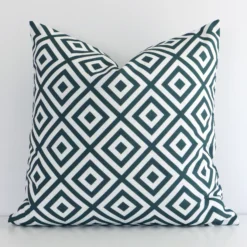 Green square cushion positioned in front of a white wall. It has geometric dimensions and is made from an outdoor material.