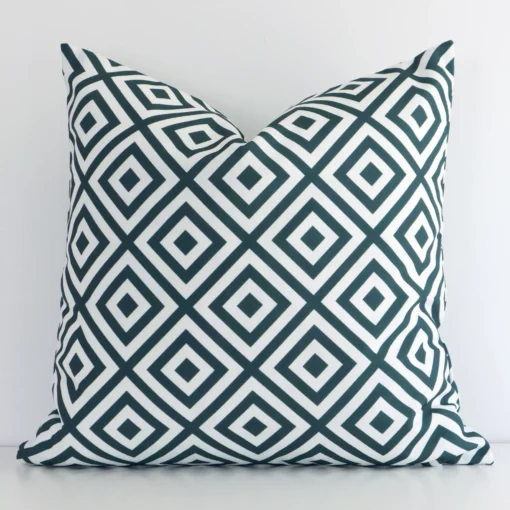 Green square cushion positioned in front of a white wall. It has geometric dimensions and is made from an outdoor material.