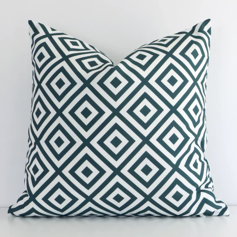 Green square cushion positioned in front of a white wall. It has geometric dimensions and is made from an outdoor material.