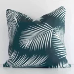 Bold square green cushion positioned in front of a white wall. Its palm style pops on the outdoor fabric.