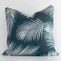 Bold square green cushion positioned in front of a white wall. Its palm style pops on the outdoor fabric.