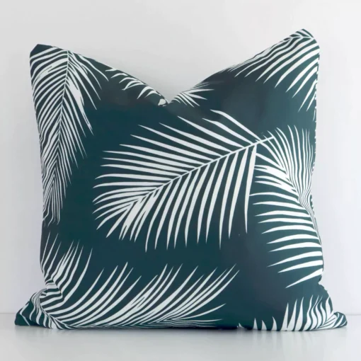 Bold square green cushion positioned in front of a white wall. Its palm style pops on the outdoor fabric.