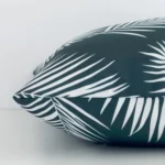Lateral angle image of an outdoor square cushion. The green colour and palm design are highlighted along its seams.