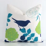 A square floral cushion in a delightful colourful tone rests against a white wall. The linen material appears to be of exceptional quality.