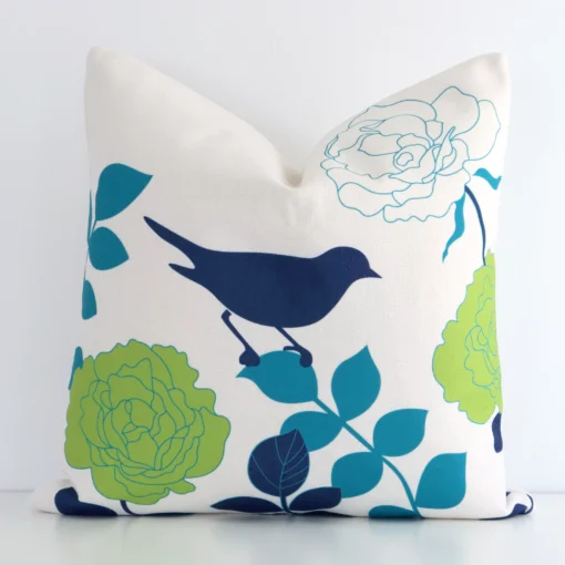 A square floral cushion in a delightful colourful tone rests against a white wall. The linen material appears to be of exceptional quality.