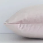 Side shot showing the seam of this rectangle dusty pink cushion that features a solid-coloured motif on its velvet material.