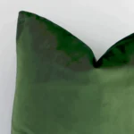 A close up shot showing the top left side of this square velvet cushion cover. The forest green tone and solid-coloured design are magnified.