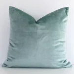 Here a mint green velvet cushion is shown styled against a white wall. It has a square design.