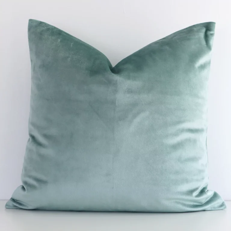 Here a mint green velvet cushion is shown styled against a white wall. It has a square design.