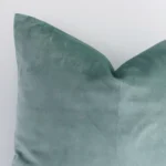 A zoomed in photo of the corner of a mint green solid-coloured cushion that has velvet fabric and a square size.