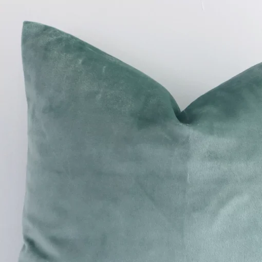 A zoomed in photo of the corner of a mint green solid-coloured cushion that has velvet fabric and a square size.