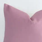 A blush linen cushion cover’s corner is shown in more detail. It is possible to see the square design and solid-coloured finish in much more detail.