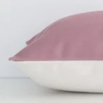 A rectangle blush cushion cover laying flat. This viewpoint highlights the solid-coloured style and linen fabric from a side position.