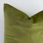 The corner of this velvet square cushion cover is shown close up. The solid colour design and olive green colour are shown in greater detail.