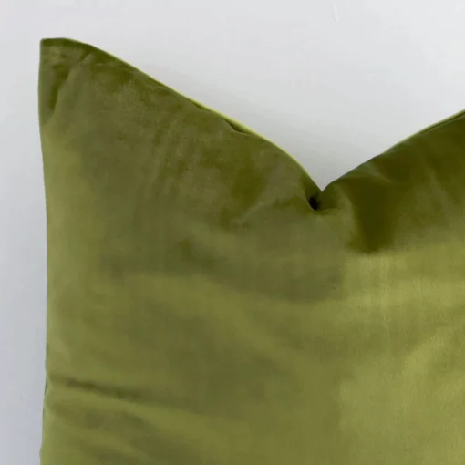 The corner of this velvet square cushion cover is shown close up. The solid colour design and olive green colour are shown in greater detail.