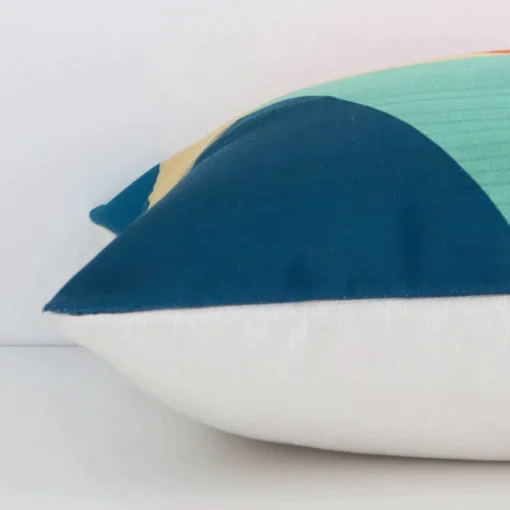 Geometric colourful cushion laid horizontally. This perspective shows the edge of the linen fabric and its square shape.