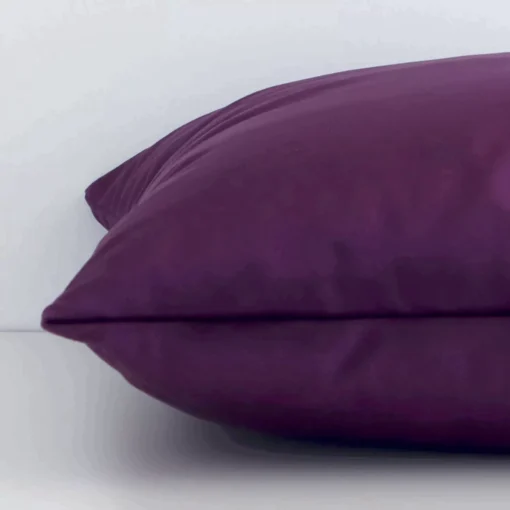 Side edge of solid-coloured square cushion. The velvet material and plum purple colour can be seen from this lateral viewpoint.