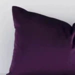 A macro image of the top left corner of this solid-coloured velvet cushion. It is possible to see the finer detail of the rectangle shape and plum purple colour.