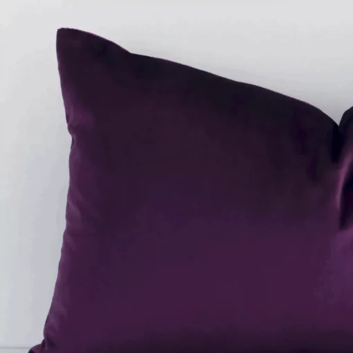 A macro image of the top left corner of this solid-coloured velvet cushion. It is possible to see the finer detail of the rectangle shape and plum purple colour.