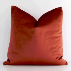 An eye-catching velvet square cushion cover featuring a hue that is rust. It has an elegant solid-coloured style.