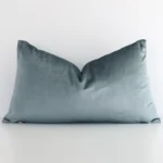 White wall with a solid-coloured sage green cushion laying against it. It has a distinctive velvet fabric and has a rectangle shape.
