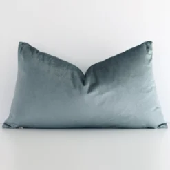 White wall with a solid-coloured sage green cushion laying against it. It has a distinctive velvet fabric and has a rectangle shape.