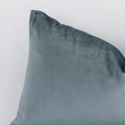 Close up view showing a corner of this solid-coloured velvet cushion in a square size and with sage green colouring.