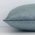 A velvet sage green cushion cover shown laying on its side. The solid-coloured design and its rectangle size are shown side on.
