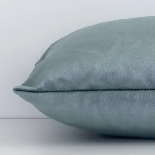 A velvet sage green cushion cover shown laying on its side. The solid-coloured design and its rectangle size are shown side on.