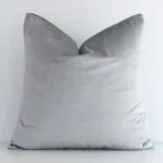 Square solid-coloured cushion cover in silver colour sitting upright in front of a brick wall. It has been made from a quality velvet material.