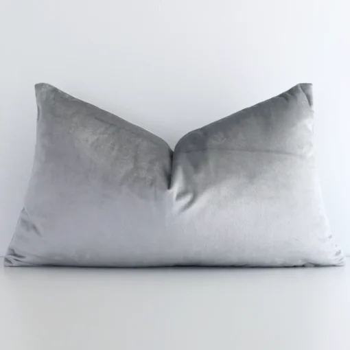 Velvet rectangle cushion with a solid-coloured design in an upright position against a white brick wall. It is silver in colour.
